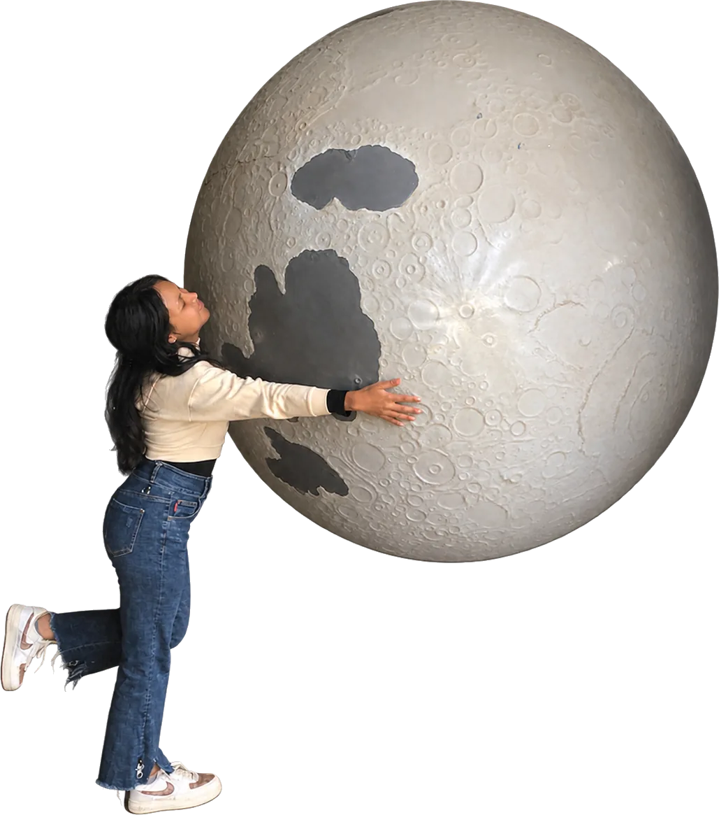 Niriantsoa enlace une grande maquette de la Lune, les yeux fermés, une jambe levée