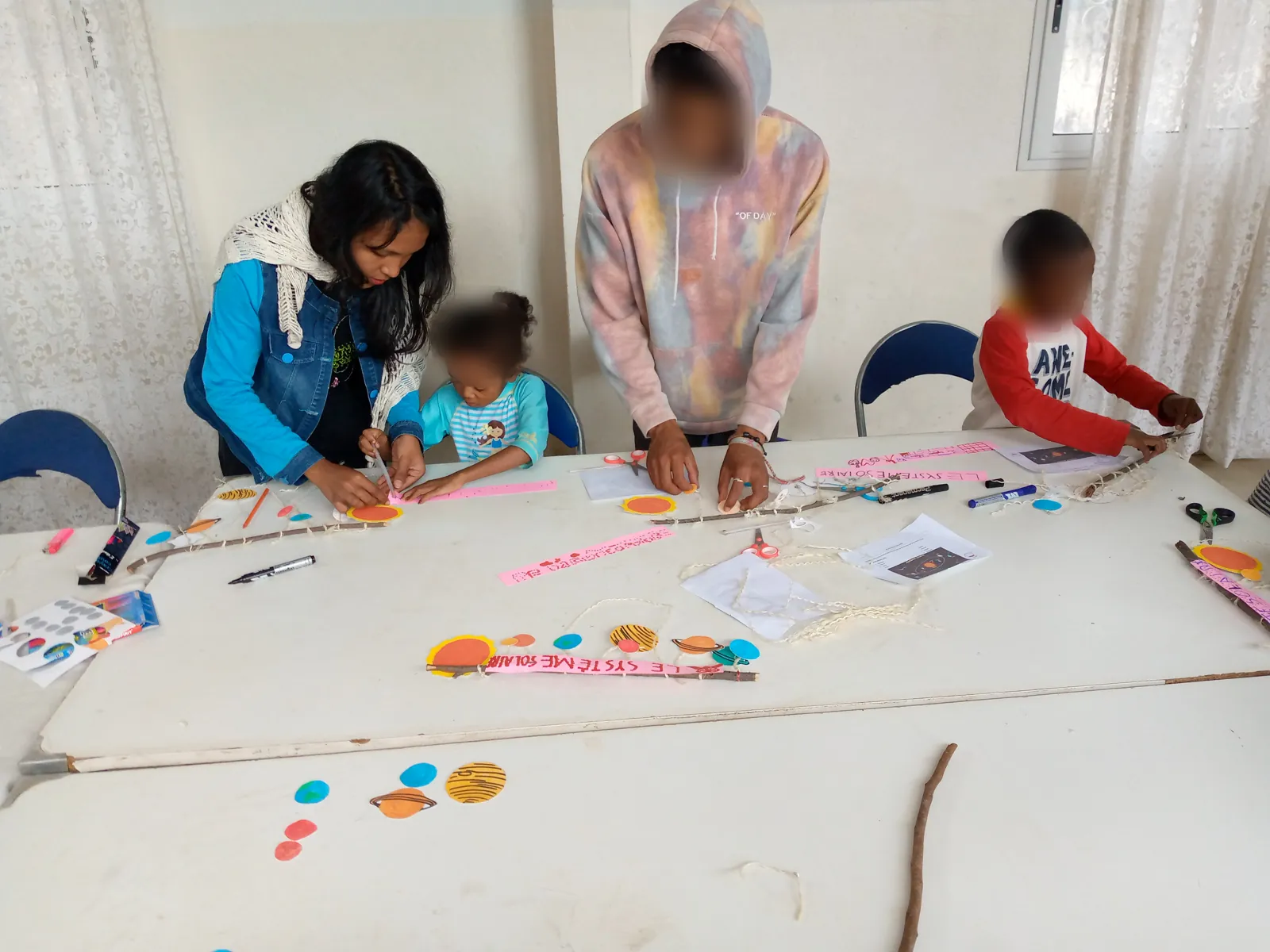 Niriantsoa aide une petite fille à assembler son système solaire en papier (visages des enfants floutés)