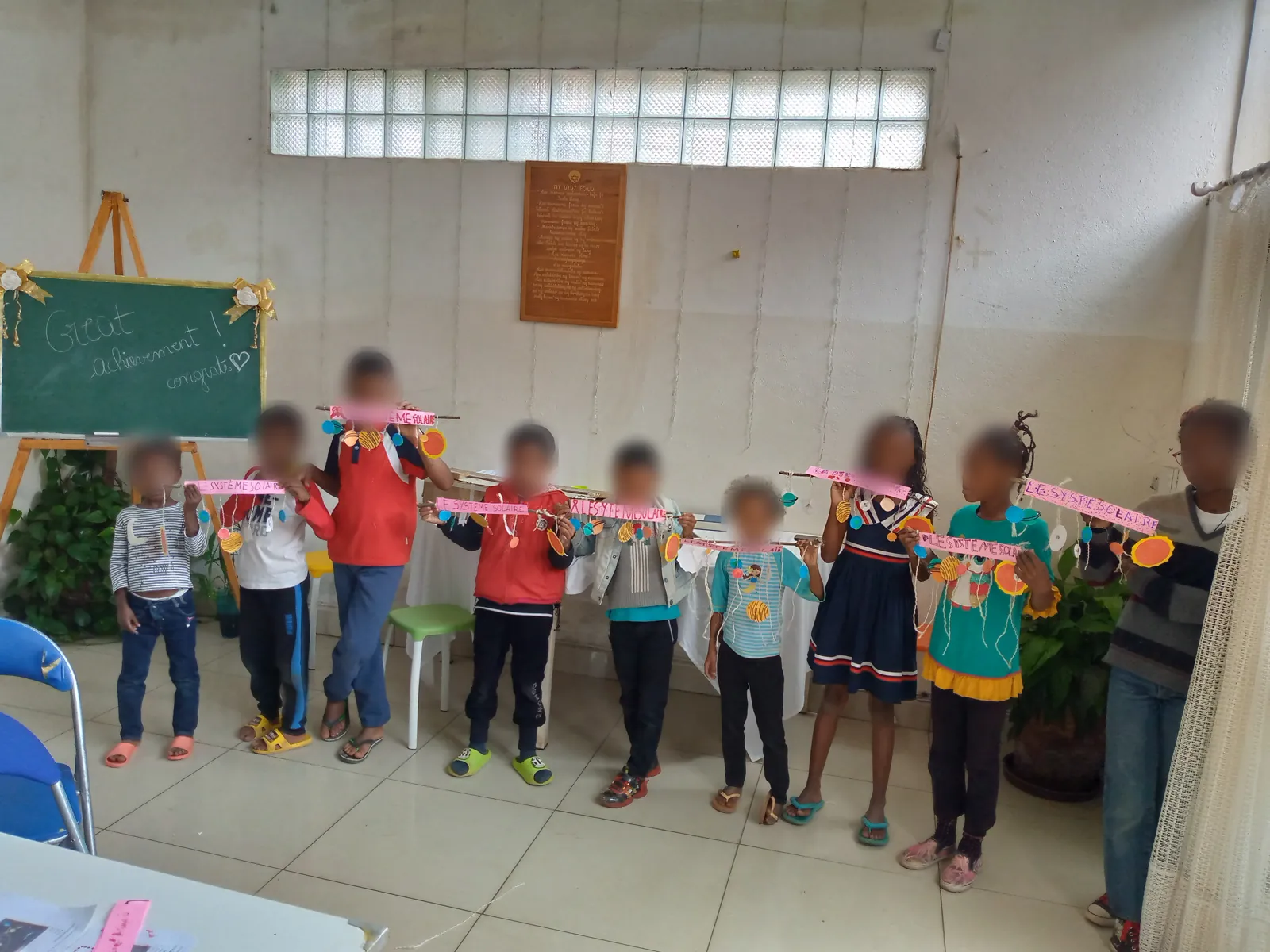 Les enfants de l'atelier montrent fièrement leur système solaire, devant un tableau « Great achievement! » (visages floutés)