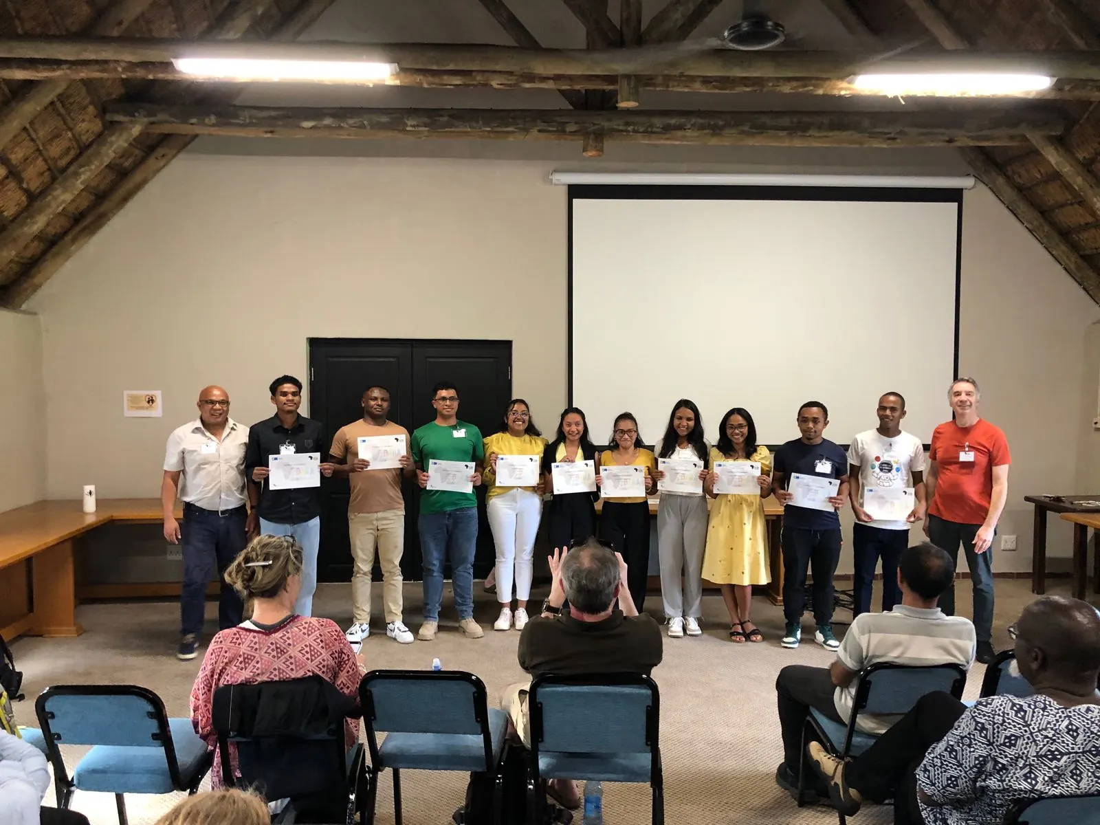La cohorte malgache DARA 2025 pose avec ses certificats, entourée de deux formateurs, devant le public