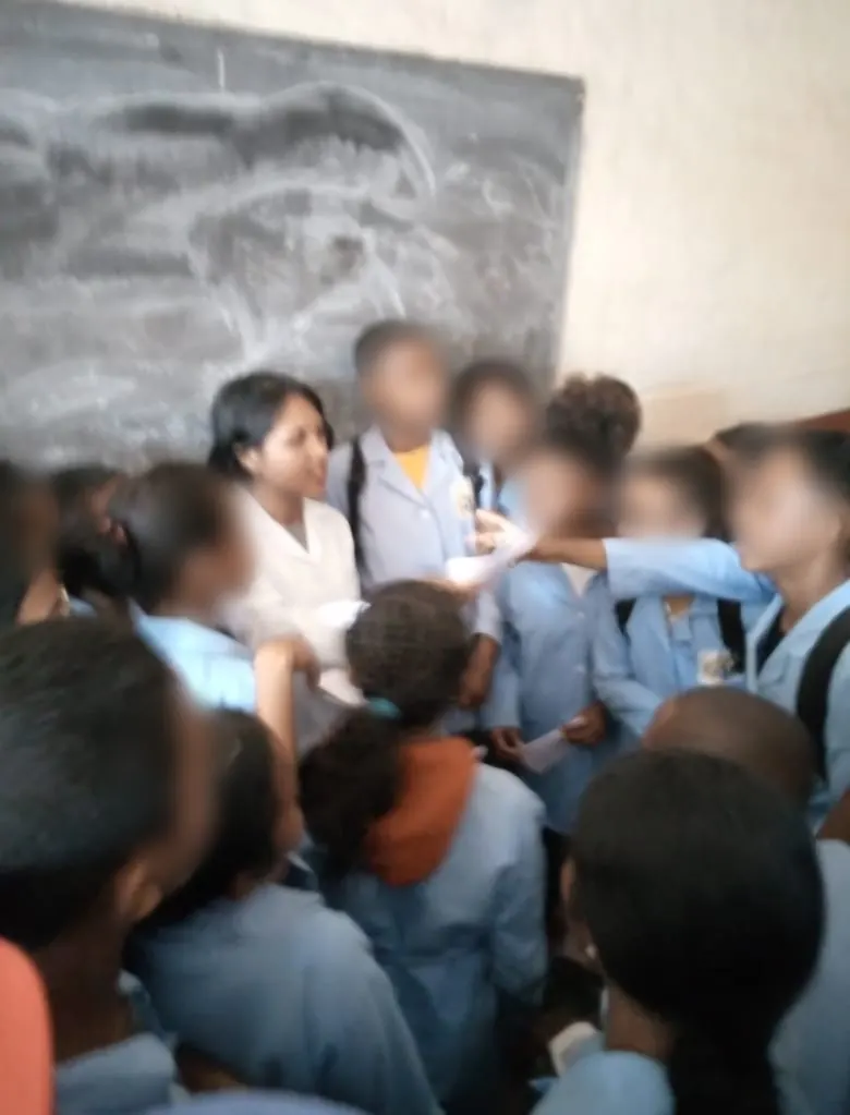 Niriantsoa en blouse, entourée de ses élèves devant le tableau (visages des élèves floutés)