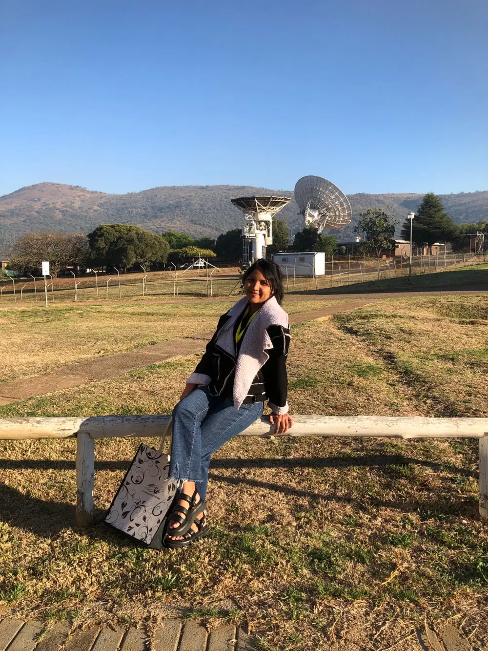Niriantsoa assise sur une barrière, avec deux antennes de l'observatoire et les collines en arrière-plan