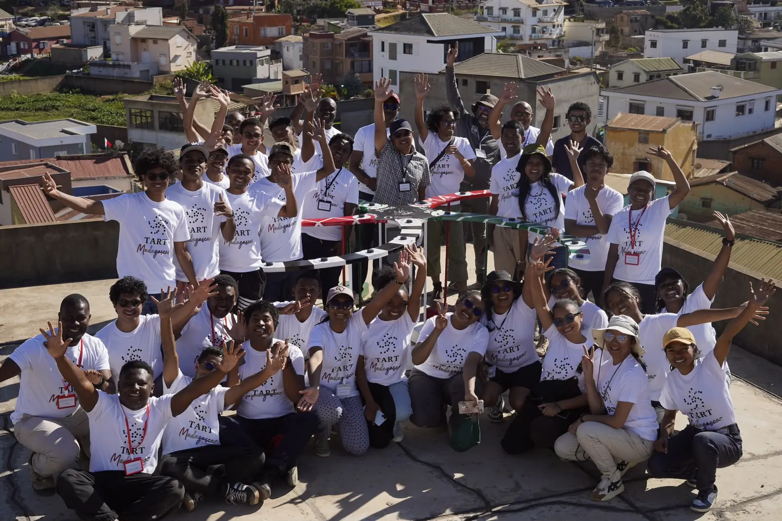 Photo de groupe des participants de TART Madagascar, bras levés, autour du télescope installé sur le toit
